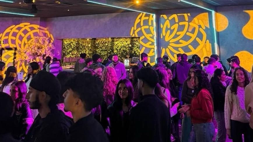 Members filling the floor at a society night, under gold mural lighting.
