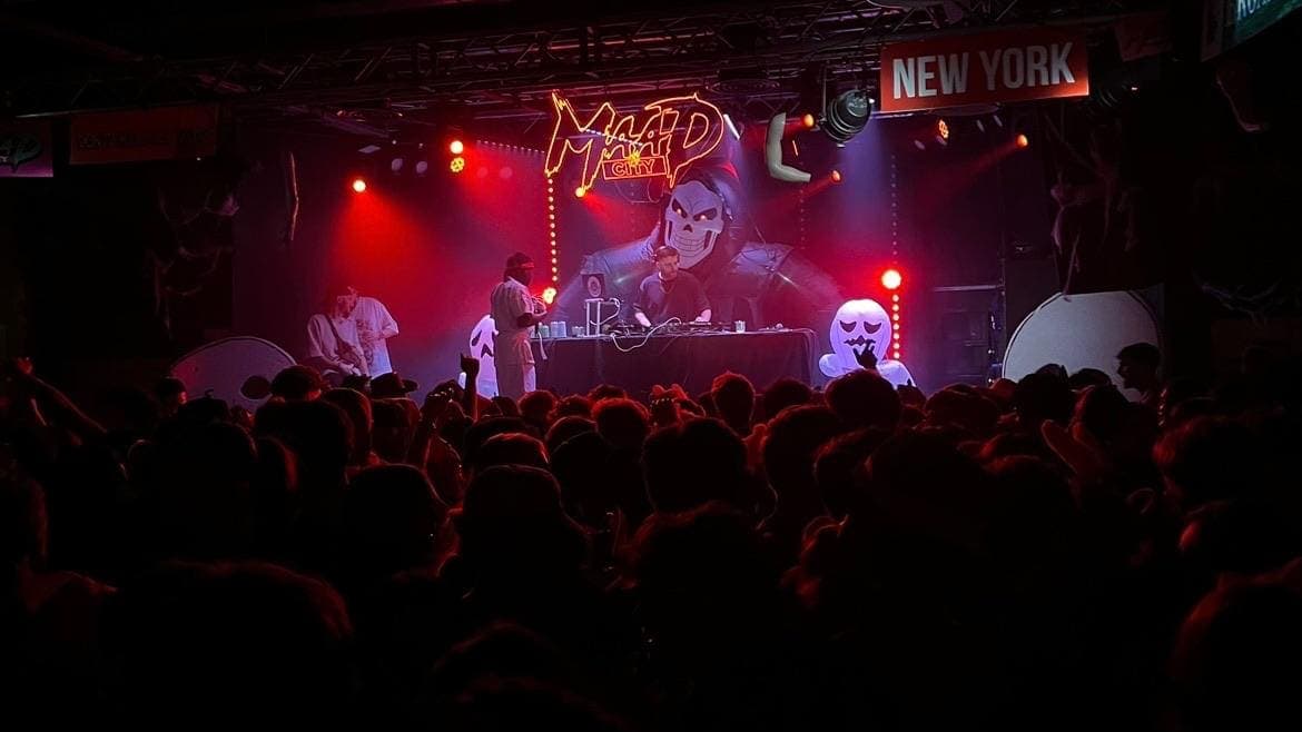 A society crowd facing the red-lit stage and DJ booth at a club night.