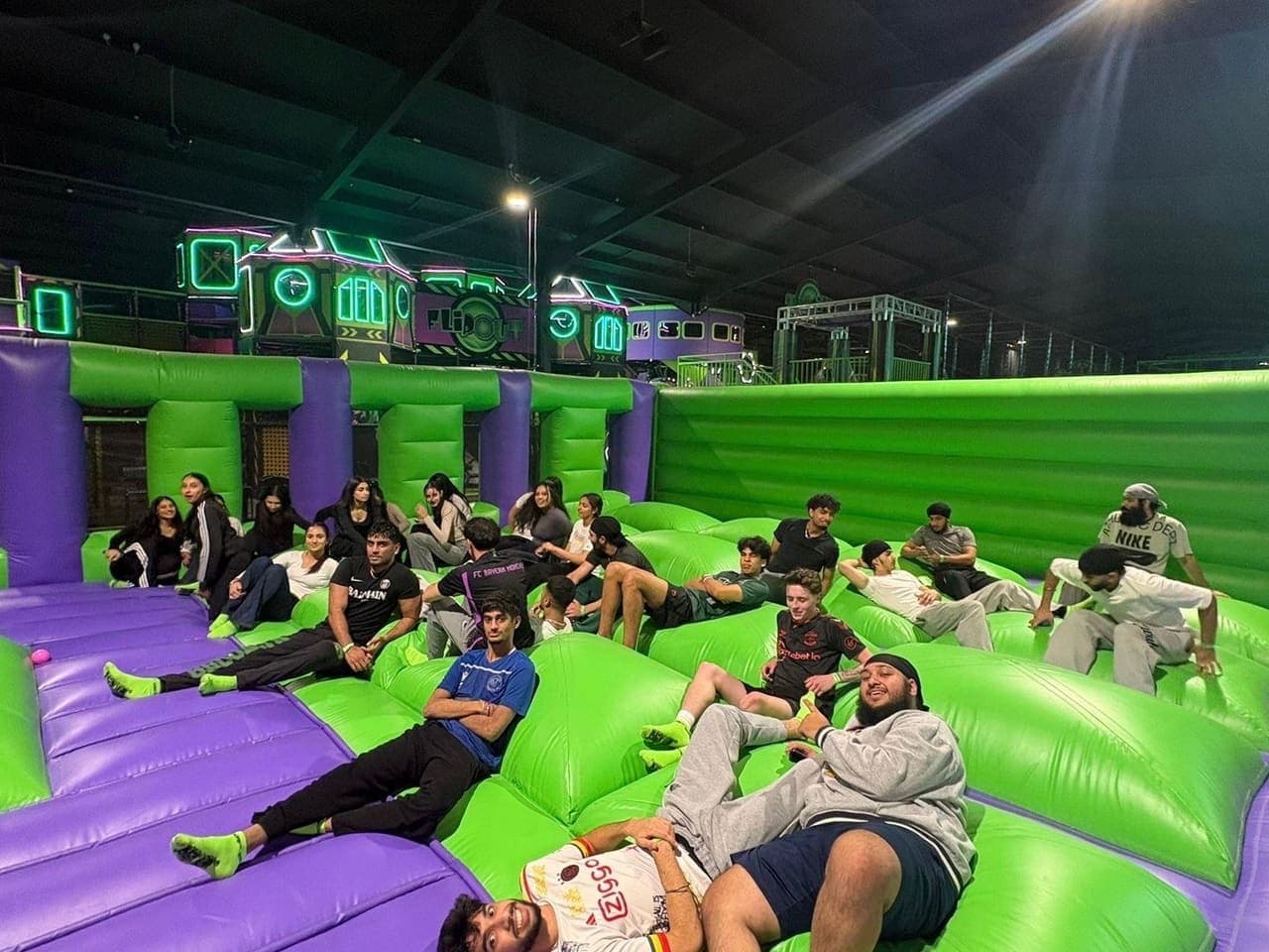 Members sprawled across green and purple inflatables at a trampoline park social.