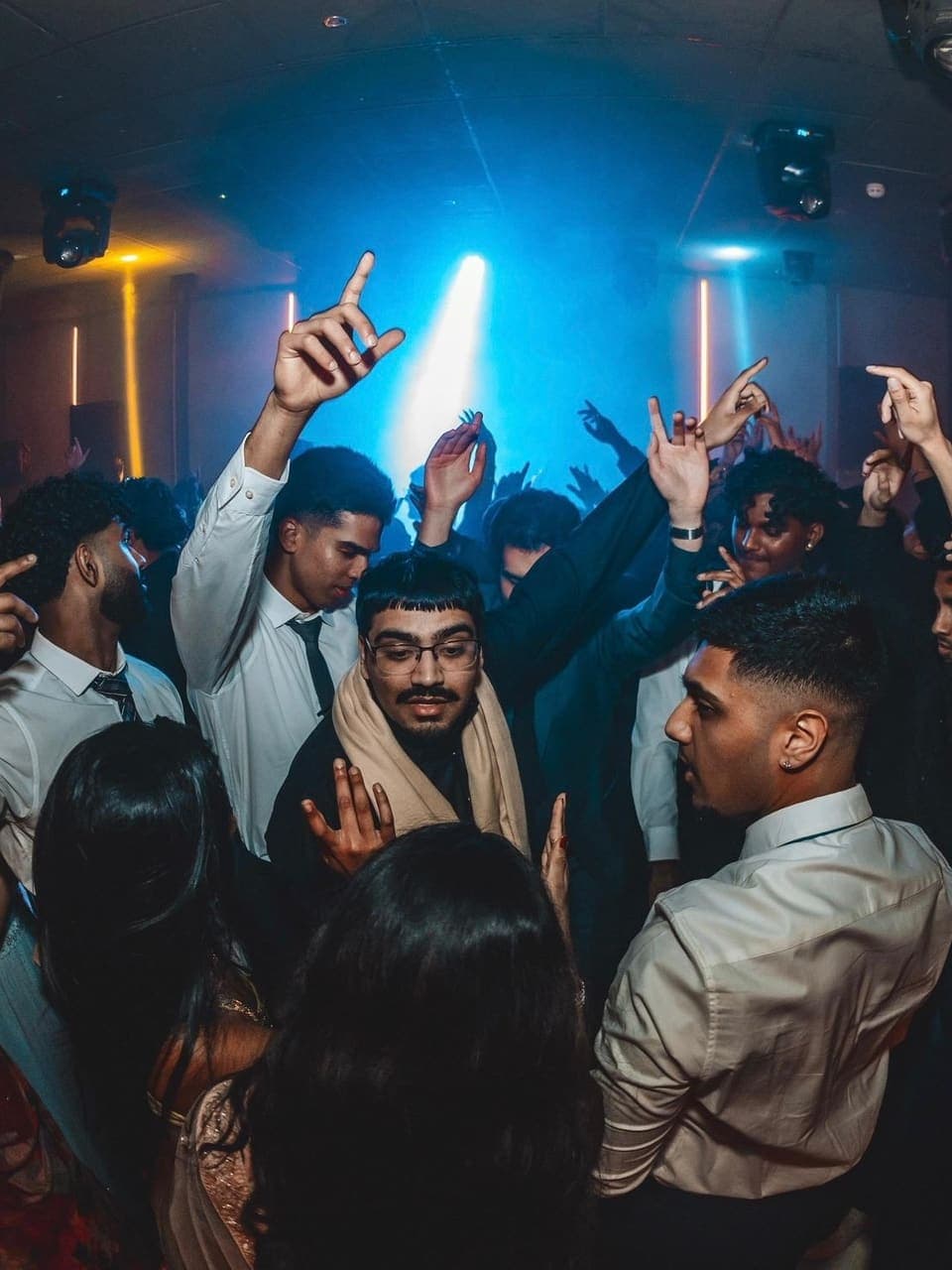 Members dancing with their hands raised under blue stage lights at a formal.