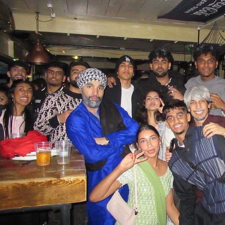 Members packed together for a photo in a pub, one in a bright blue kurta.